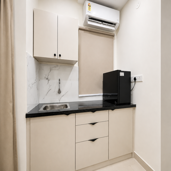 Compact kitchen, modern kitchen, kitchenette, contemporary interior, minimalist kitchen, small kitchen, modular kitchen, kitchen cabinets, overhead cabinets, lower cabinets, beige cabinets, black countertop, granite countertop, kitchen sink, stainless steel sink, faucet, marble backsplash, white marble, kitchen appliance, microwave oven, air conditioner, window, roller blind, beige curtain, neutral colors, cream walls, tiled floor, storage cabinets, kitchen drawers, cabinet handles, black accents, clean kitchen, functional kitchen, apartment kitchen, residential interior, compact living, space-saving design, modern home, elegant interior, simple decor, contemporary furniture, organized kitchen, bright interior, soft lighting, indoor photography, home improvement, kitchen design, sleek countertop, wall-mounted AC, window treatment, neutral palette.